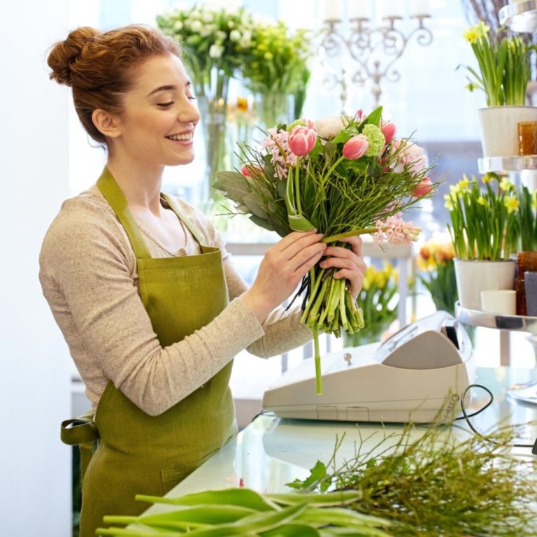Femme souriante arrange des fleurs dans une boutique.