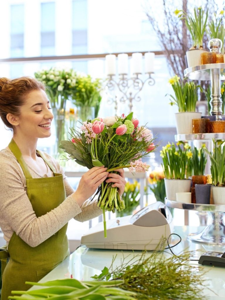 Femme souriante dans une fleuriste, tenant un bouquet de fleurs.